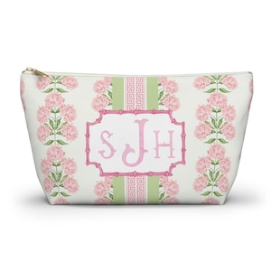 Puede incluir: Un estuche con cremallera sobre fondo blanco con rayas verticales de flores de hortensia rosas y detalles verdes. Un marco central rosa estilo bambú contiene las letras del monograma SJH en rosa claro sobre una franja verde claro.