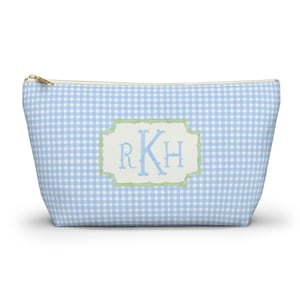 Op de afbeelding: Een toilettas met blauw en wit geruit patroon en een gouden ritssluiting. De tas heeft een lichtblauw monogram met de letters RKH in een groen bamboe-achtig frame. De tas is lichtblauw.