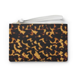 May include: A rectangular clutch with a tortoiseshell pattern in shades of brown and black. The clutch has a white wrist strap and a gold zipper. The accessory is designed for carrying essentials.