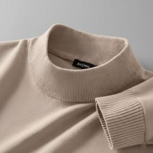 May include: A close-up of a beige turtleneck jumper. The ribbed collar and cuffs are visible, with the word "ANIMAL" on a small black label. The jumper is made of a soft, knit material.