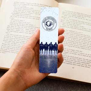 May include: A white bookmark featuring the Briar University Hawks logo and the silhouettes of hockey players. The numbers 44, 22, 66, and 46 are visible on the bookmark. The bookmark is held over an open book.