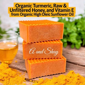 May include: Three rectangular orange soap bars stacked vertically. The text reads: Organic Turmeric, Raw & Unfiltered Honey, and Vitamin E from Organic High Oleic Sunflower Oil. The middle bar features the white cursive text A and Shay.