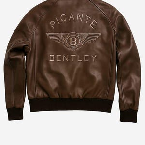 Puede incluir: Chaqueta bomber de cuero marr&oacute;n con la palabra "PICANTE" arqueada en la espalda, encima de un emblema alado y la palabra "BENTLEY". La chaqueta tiene dobladillo y pu&ntilde;os de canal&eacute;. El logotipo de Etsy est&aacute; en la parte inferior.