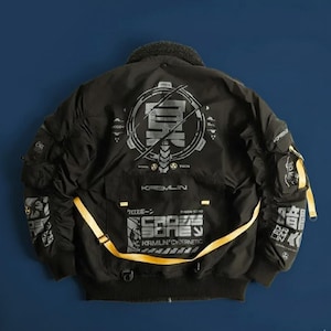 May include: Black bomber jacket with a faux fur collar and multiple pockets. The jacket features graphic designs in gray and yellow, including text that reads "KREMLIN" and "CROSS BONE". A yellow strap accents the front.