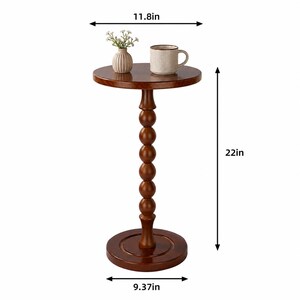 Op de afbeelding: Een ronde bruine houten bijzettafel met een spilvormige voet. De tafel heeft een diameter van 29,97 cm aan de bovenkant, 23,8 cm aan de basis en een hoogte van 55,88 cm. Een kleine witte vaas met bloemen en een mok staan op het oppervlak.