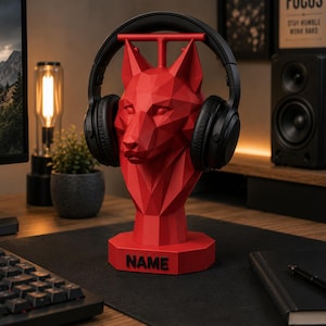 May include: A red, geometric, low-poly wolf head sculpture serving as a headphone stand. The sculpture features a flat, octagonal base with the word NAME embossed in black lettering. A pair of black over-ear headphones rests on the wolf's ears.
