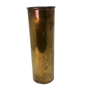 May include: A tall, cylindrical brass vase with a slightly flared top. The vase has a warm, golden hue with visible patina and minor surface imperfections, suggesting age and use. The design is simple and elegant, suitable for displaying flowers or as a decorative item.