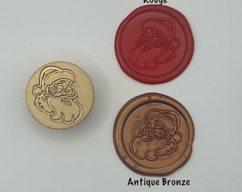 May include: A brass Santa Claus wax stamp next to two wax seals. One seal is red with the word "Rouge" above it, and the other is antique bronze with the words "Antique Bronze" below it. The Santa Claus design is embossed on each item.