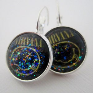 May include: A pair of silver dangle earrings with black and yellow round glass charms featuring the Nirvana logo and a smiley face with glitter.