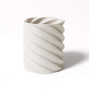 Peut inclure: Un vase cylindrique blanc avec un motif tourbillonnant texturé. Le vase présente un motif nervuré qui s'enroule autour de son corps. Le design rappelle une colonne torsadée. Le vase est fait d'un matériau solide et opaque.