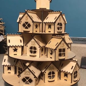 May include: A multi-tiered wooden advent calendar in the shape of a village. Each small house is numbered from 1 to 24, with decorative windows and cut-out details. The natural wood colour gives it a rustic appearance.