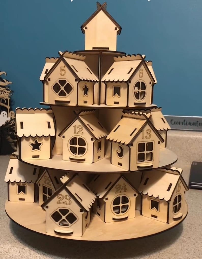 May include: A multi-tiered wooden advent calendar in the shape of a village. Each small house is numbered from 1 to 24, with decorative windows and cut-out details. The natural wood colour gives it a rustic appearance.