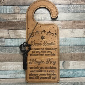 May include: Wooden door hanger with a decorative key. The sign reads "Dear Santa, we have no chimney as you can see, please just use this Magic Key..." with reindeer and star accents. A black key hangs from the sign.
