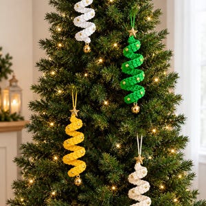 May include: Four spiral-shaped crochet ornaments hanging on a Christmas tree. Each ornament features a white, green, or yellow yarn structure, a gold-colored star at the top, small gold beads along the spiral, and a gold bell at the bottom.