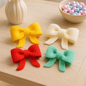 Può includere: Quattro fiocchi all'uncinetto fatti a mano, gialli, bianchi, rossi e verdi, sono appoggiati su una superficie di legno. Un vaso di fiori bianchi e una ciotola di perline pastello sullo sfondo. I fiocchi sono un affascinante oggetto artigianale.