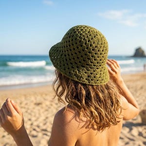 Peut inclure: Un chapeau vert en crochet avec un large bord. Le chapeau est porté par une personne sur une plage de sable, avec l'océan et le ciel bleu en arrière-plan. Le chapeau est fait d'un matériau texturé à tissage ouvert.