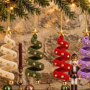 May include: Four spiral-shaped Christmas tree ornaments made of crocheted yarn in cream, olive green, red, and purple. Each ornament features small gold beads attached along the spiral and is topped with a gold star, hanging from a gold string.