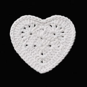 May include: A white, crocheted heart-shaped item against a black background. The heart is made of white yarn, with a textured surface and visible stitch patterns. The edges are neatly defined, and the overall shape is symmetrical.