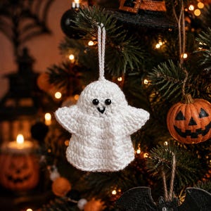 Puede incluir: Un adorno de fantasma tejido a ganchillo en color blanco con dos pequeños ojos de plástico negro y una boca bordada en negro. El fantasma tiene una cabeza redondeada y brazos extendidos, con un lazo de hilo blanco para colgar.