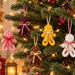 May include: Five crocheted gingerbread-style ornaments hanging on a Christmas tree. The figures are pink, dark red, yellow, brown, and white. Each ornament features a small bow at the neck and a looped string for hanging in various striped patterns.