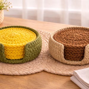 K&ouml;nnte beinhalten: Zwei handgefertigte H&auml;keluntersetzer-Sets. Ein Set hat einen gelben Untersetzer mit einem gr&uuml;nen Halter, das andere einen braunen Untersetzer mit einem beigen Halter. Beide Sets befinden sich auf einer gewebten Tischmatte, ideal f&uuml;r die Inneneinrichtung.