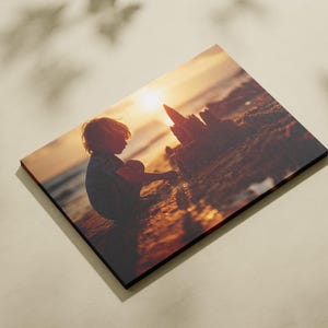 May include: A rectangular wooden print showing a child silhouetted against a sunset, constructing a sandcastle on a beach. The image has warm orange and brown tones, with a black border.