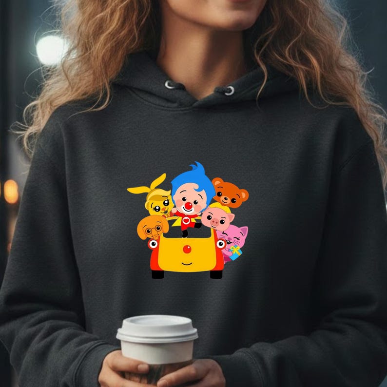 May include: A dark gray hoodie featuring a colorful graphic of cartoon characters in a yellow vehicle. The graphic includes a clown with blue hair and a red nose, along with several animal characters. The hoodie has a drawstring hood.