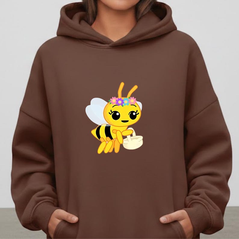 May include: Brown hooded sweatshirt featuring a cartoon bee with a flower crown and a small basket. The bee is yellow and black with white wings. The sweatshirt is a solid brown color.