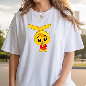 May include: White t-shirt featuring a cartoon rabbit character with yellow ears, hair, and a red outfit. The rabbit has large, expressive eyes and a friendly expression. The shirt is a casual, everyday wear item.