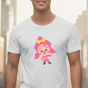 May include: White t-shirt featuring a cartoon character in a pink outfit with a yellow bow. The character has rosy cheeks and a smiling expression. The design is centered on the shirt.