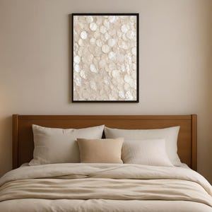 Puede incluir: Una pieza de arte mural rectangular con un patrón denso y superpuesto de discos de concha blancos iridiscentes en un marco negro, colocada sobre un cabecero de madera con almohadas beige y una funda nórdica beige a juego en una cama.
