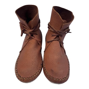 Peut inclure: Une paire de bottines en cuir marron texturé. Ces chaussures présentent une construction souple et flexible avec un bout arrondi, une couture apparente en point de surjet le long de la semelle et de fins lacets en cuir qui s'enroulent autour de la cheville.