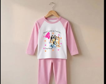May include: A two-piece pyjama set with a white long-sleeve top featuring pink raglan sleeves and a graphic of the Bluey family, the number 4, and the text "When I wake up I will be..." and "Ivy-Rose". The set includes matching pink trousers.