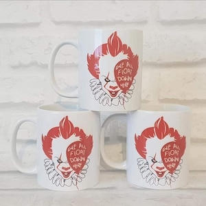 May include: Three white ceramic mugs featuring a red graphic of a clown face with a ruffled collar. A red balloon shape covers part of the clown's face with the text WE ALL FLOAT DOWN HERE printed in white letters inside the balloon graphic.