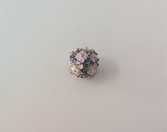 May include: A silver charm bead with a floral design. The bead is covered in small, colorful flowers in shades of pink, blue, green, and yellow. The flowers are arranged closely together, creating a textured surface.