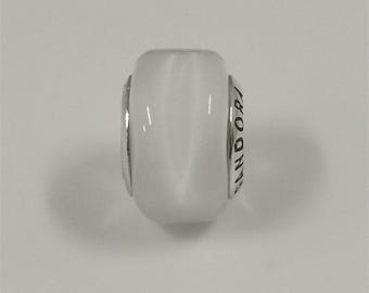 May include: A white, cylindrical bead with silver-colored accents. The bead has the word "PANDORA" engraved on one side. The bead is smooth and reflective, with a glossy finish. The bead is likely a charm for a bracelet or necklace.