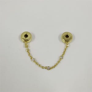 Può includere: Una catena di sicurezza per gioielli color oro con due chiusure rotonde e una delicata catena ornata da piccole gemme trasparenti. La catena è progettata per proteggere i gioielli.