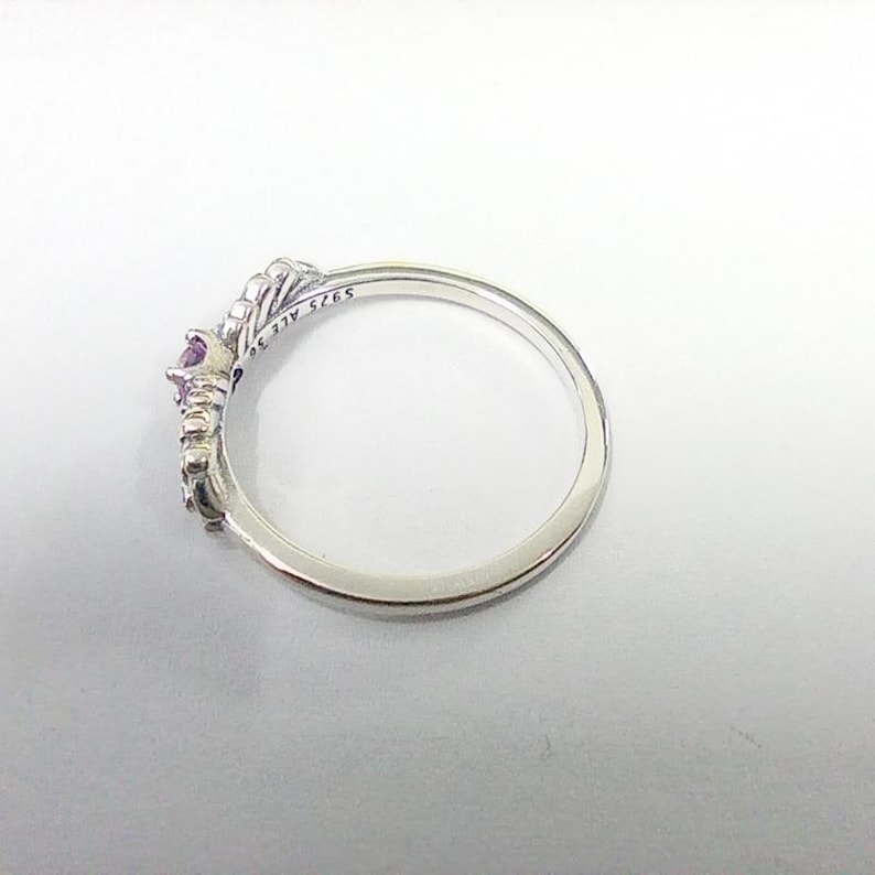 May include: A silver ring with a crown design, featuring a central purple gemstone and smaller accent stones. The ring is marked with "S925 ALE 56". The ring is set against a white background.