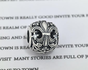 May include: A silver charm with a fleur-de-lis design, adorned with small clear crystals. The charm has an intricate, detailed pattern and is likely made of sterling silver. The design is a classic symbol, suitable for a bracelet or necklace.