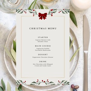 May include: A Christmas menu card with a festive design. The card features a cream background with a gold border and a red bow at the top. The menu includes starter, main course, dessert, and drink options.