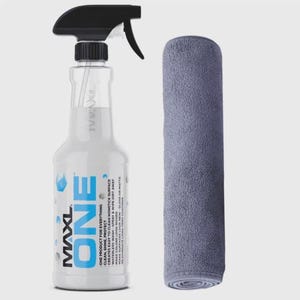 May include: A clear spray bottle with a black trigger and the word "ONE" in large blue letters. Next to it is a rolled-up gray microfiber cloth. The bottle has text that reads "ONE PRODUCT FOR EVERYTHING".