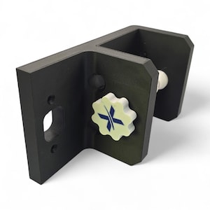 Pu&ograve; includere: Una staffa nera ad angolo retto con una manopola bianca a forma di stella con un design a croce blu. La staffa ha un'apertura rettangolare e un componente bianco a forma di sfera. L'oggetto &egrave; posto su uno sfondo bianco.