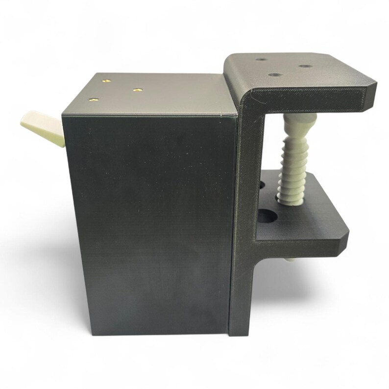 Pu&ograve; includere: Un morsetto nero stampato in 3D con un meccanismo a vite bianco e una piccola leva bianco sporco. Il morsetto ha una base rettangolare e una piattaforma superiore con quattro fori. Il design &egrave; moderno e funzionale.