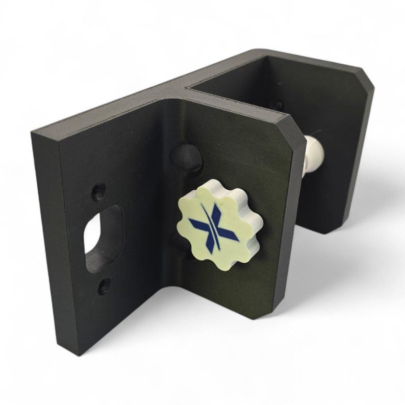 Peut inclure: Un support de montage en forme de L noir mat dot&eacute; d'une ouverture circulaire et d'un bouton de r&eacute;glage blanc en forme d'engrenage. Le bouton est orn&eacute; d'un logo bleu en forme de X. Le support pr&eacute;sente une structure angulaire robuste.