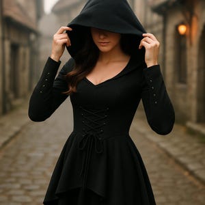 May include: Black hooded dress with a corset-style bodice and flared skirt. The long-sleeved dress features decorative buttons on the cuffs. The hood is pulled up, partially obscuring the face. The dress is made of a dark fabric.