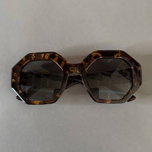 May include: Tortoise shell sunglasses with a geometric octagon frame and dark lenses.