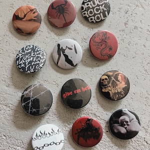 Puede incluir: Una colección de once chapas redondas con diversos diseños gráficos, incluyendo un escorpión, un dragón, calaveras, alambre de espino, cadenas, llamas y textos como "sex drugs rock roll" y "give em hell" en negro, rojo y blanco.
