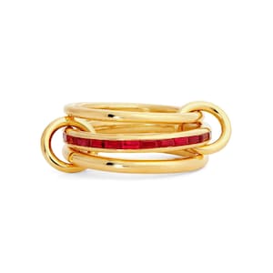 May include: A gold-colored ring with three interlocking bands. One band is adorned with a row of small, rectangular red gemstones. The ring has a polished finish and a modern design, suitable for everyday wear or special occasions.