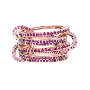 May include: A stack of rose gold rings with a continuous design. Each ring is encrusted with small, round, pink gemstones. The rings are interlocked, creating a unique and eye-catching piece of jewelry.
