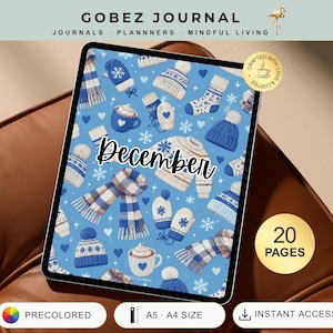 May include: A digital tablet displaying a December journal cover with a blue background featuring illustrations of winter clothing including sweaters, scarves, mittens, hats, socks, and mugs of hot cocoa with the text December in black script.